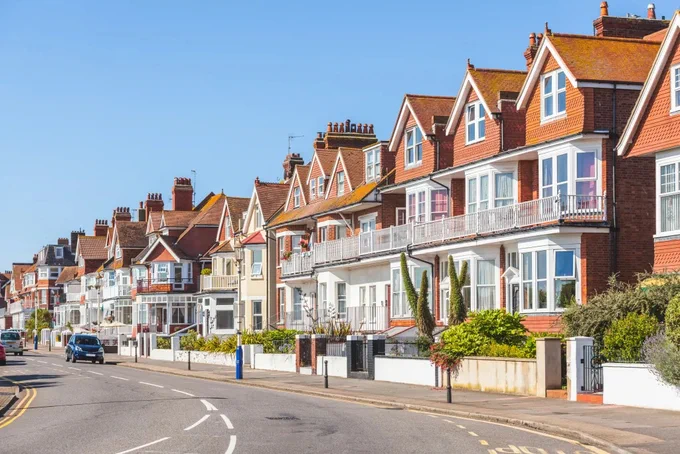 Row of charming seaside houses with red-tiled roofs and large windows under a clear blue sky.