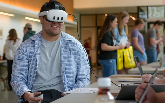 A male student wears virtual reality goggles during the 2025 Scholar Symposium as he experiences a video game developed by a 