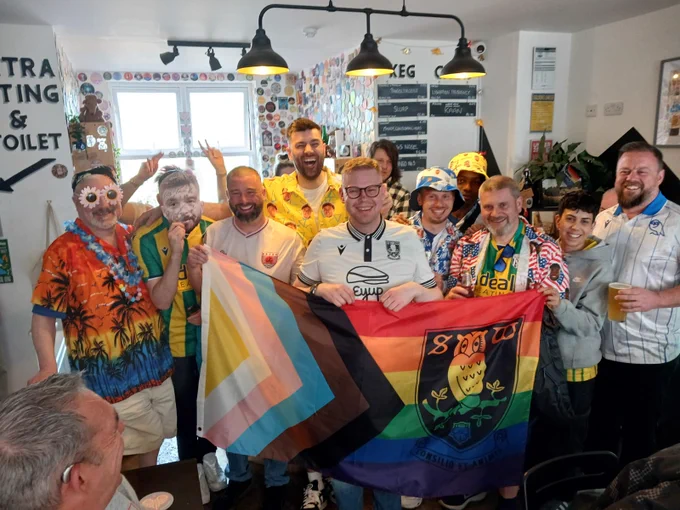 A photo of several Proud Baggies and Rainbow Owls members holding SWFC's Progress Pride flag at The Pangolin.
