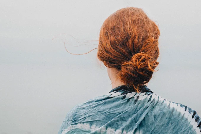 Young woman with red hair, shown from behind, looking into the distance