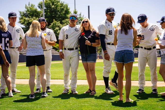 Players stand with their moms on the field, taking photos together before first pitch.