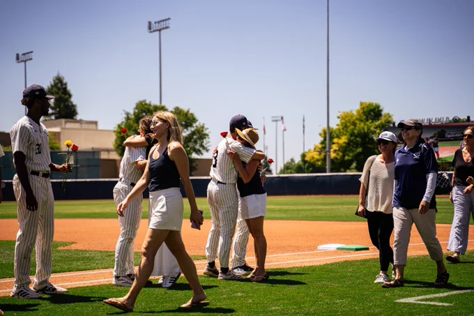 A player hugging his mom along the foul line as families walk the field together.