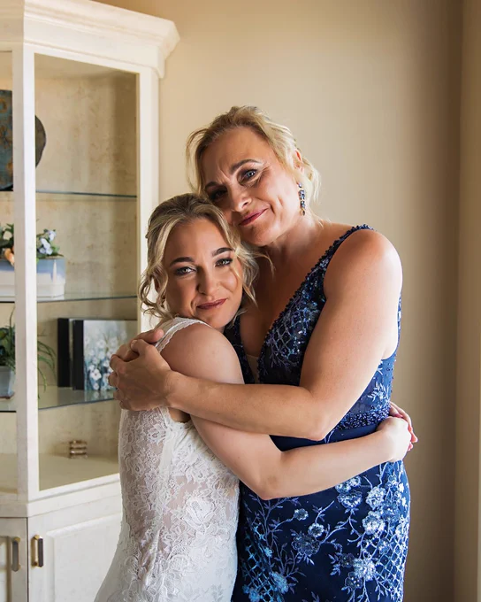 A photo of a bride and her mother hugging and smiling on her wedding day.