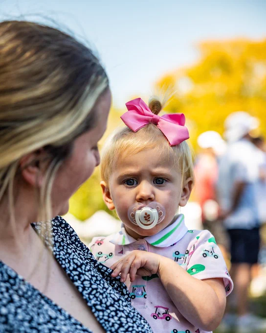 A photo of a little girl in a golf outfit with a pink bow in her hair with her mom holding her and smiling.