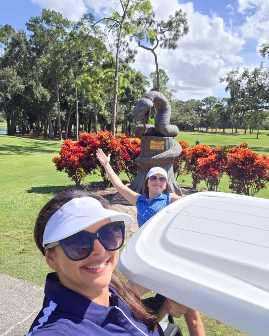 A selfie of a mom and her teenage daughter on a golf cart with the Snake Pit Statue in the background.