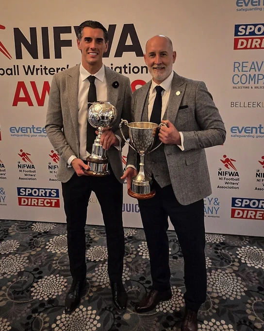 Two men in suits holding trophies at the NI Football Writers' Association Awards. The mood is celebratory and formal.