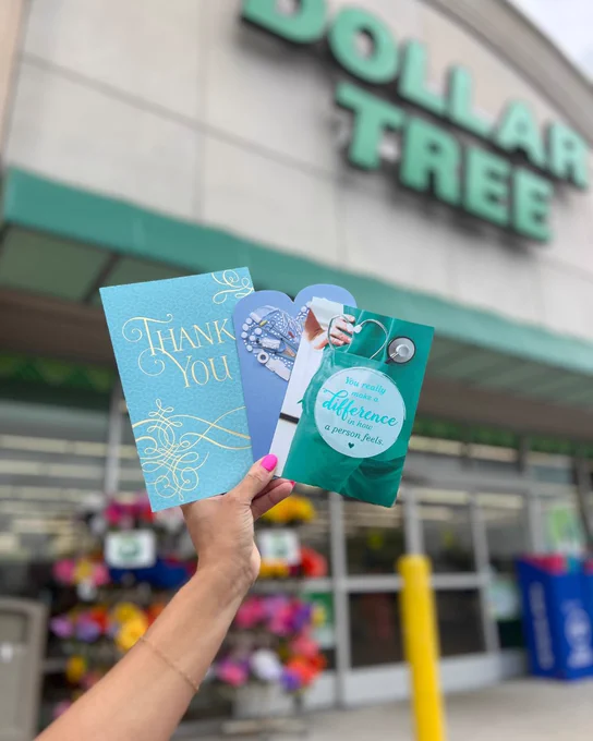 Hand holding three thank you cards in front of a Dollar Tree store entrance with colorful flowers visible inside.