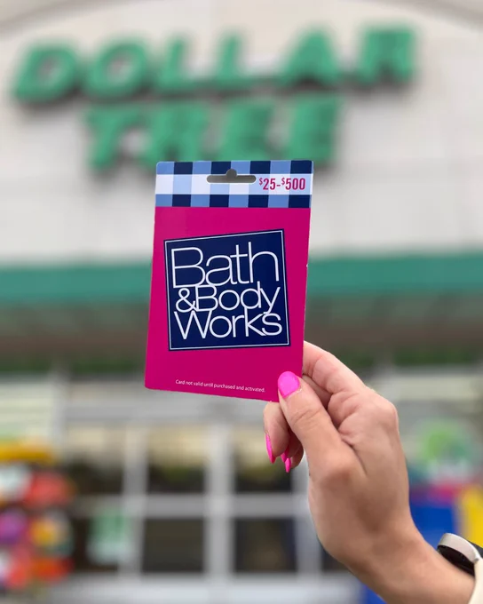Hand holding a Bath & Body Works gift card with a $25-$500 value in front of a Dollar Tree store entrance.