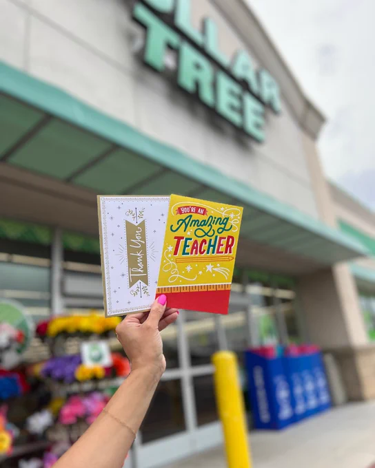 Hand holding two colorful greeting cards outside a Dollar Tree store, one card says 'Thank You' and the other 'You're an Amazing Teacher'.