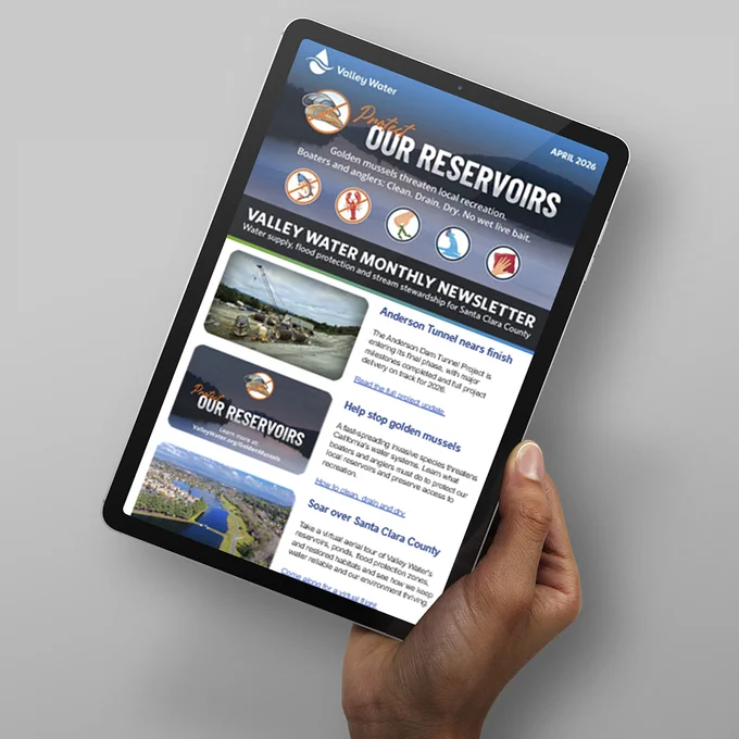 Hand holding a tablet displaying Valley Water's monthly newsletter with articles about local reservoirs, completion of Anderson Tunnel, and water conservation.