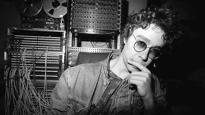The late great Karl Wallinger of World Party, photographed in a stripped-back studio setting circa 1990, surrounded by analogue gear and wiring — a quiet, focused presence that mirrors the introspective and crafted sound of the Goodbye Jumbo era.