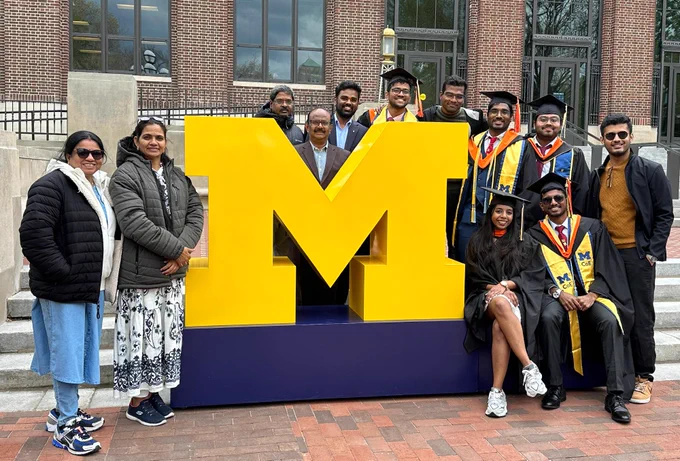 Large group of grads and their family members surround a giant block M.