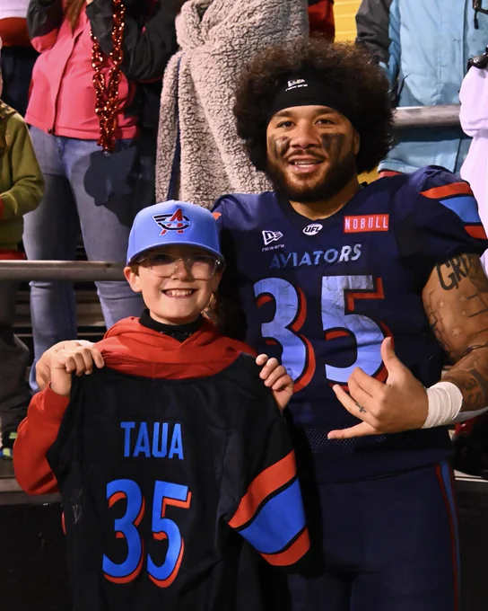 A football player poses with a young fan holding a jersey. The photo conveys a cheerful and celebratory mood.