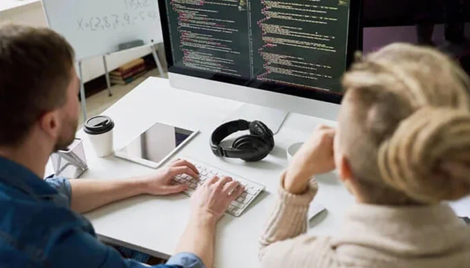 Startup developers reviewing Java code on desktop screens while discussing trusted Java development outsourcing partners for 2026.