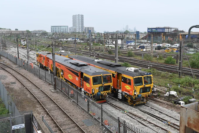 A photo of a pair of tamping trains at Willesden on the West Coast Main Line - Tamping machines restore the line and level of the track and we use them after work to alter or renew sections of track. They insert large tools called tines into the ballast – the stones beneath the track – and then force the tines together to move ballast under the sleepers. The tamping machine moves additional ballast under the sleepers to raise the height of the track and can move the track sideways if required.