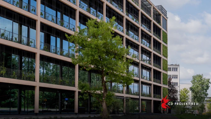 Glass exterior of a CD PROJEKT RED building featuring floor-to-ceiling windows and plants growing vertically along wires.