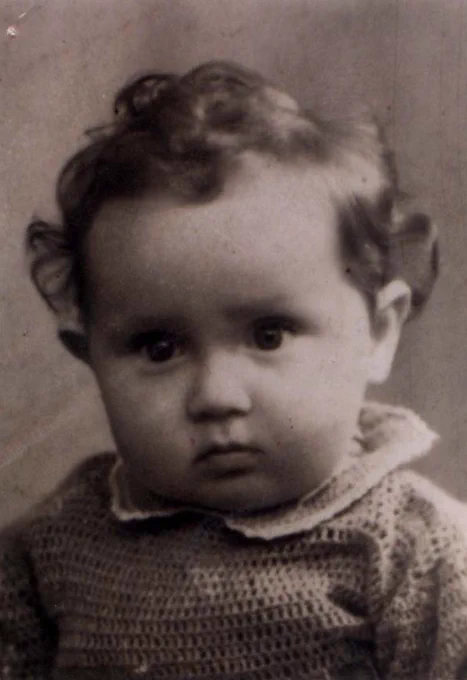 A portrait photo of the face and shoulders of a very young girl. She has curly hair. She is wearing a sweater with a collar.