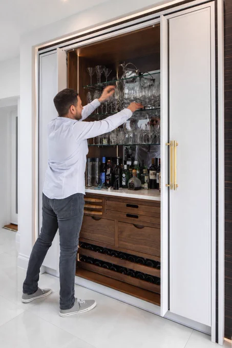 Man in home organising wine glasses in his kitchen bar cupboard with pocket doors