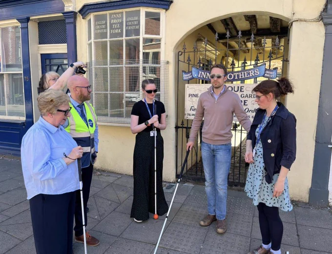 Photo from Press showing Luke Charters wearing sim specs and holding a long white cane.