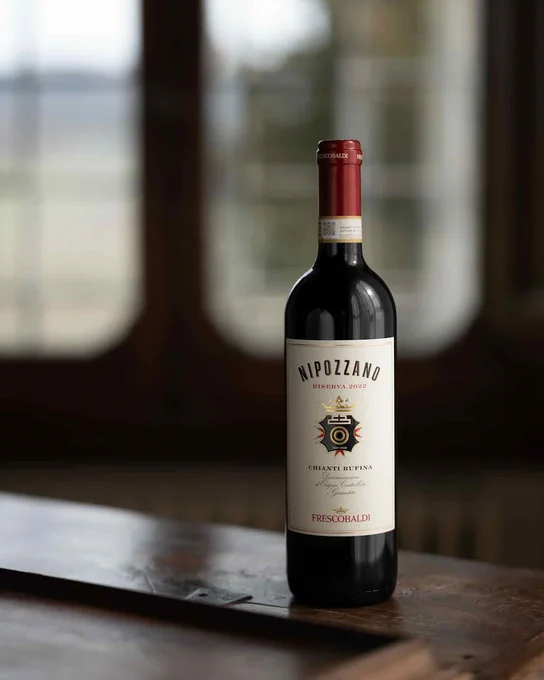 Single bottle of red wine “Nipozzano Riserva” standing on a wooden surface, full label visible with Marchesi Frescobaldi crest and wine name, premium Italian red wine presentation.
