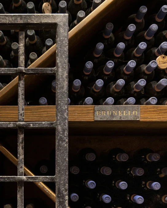 Interior of a wine cellar with stacked wooden racks filled with dark wine bottles of Brunello di Montalcino resting horizontally, professional aging of Marchesi Frescobaldi wines at Tenuta CastelGiocondo, Tuscany.
