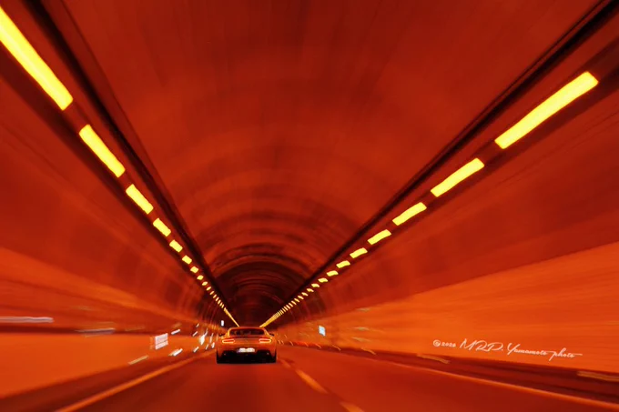 ALT : ⬇️  

A motion-blur photograph from a low-angle perspective (from the passenger front seat behind the hub who takes on the wheel) —behind a white car driving through a brightly lit tunnel. The ceiling lights create symmetrical orange lines that converge toward the center, emphasizing speed and travel.

Location: 東北自動車道 • 宮城県辺り

©2026 MRP. Yamamoto | photographié