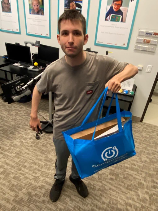 Young man standing in computer lab holding a blue bag 