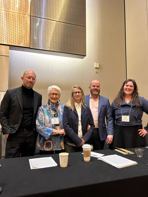 Five panelists stand behind a table. End ID.