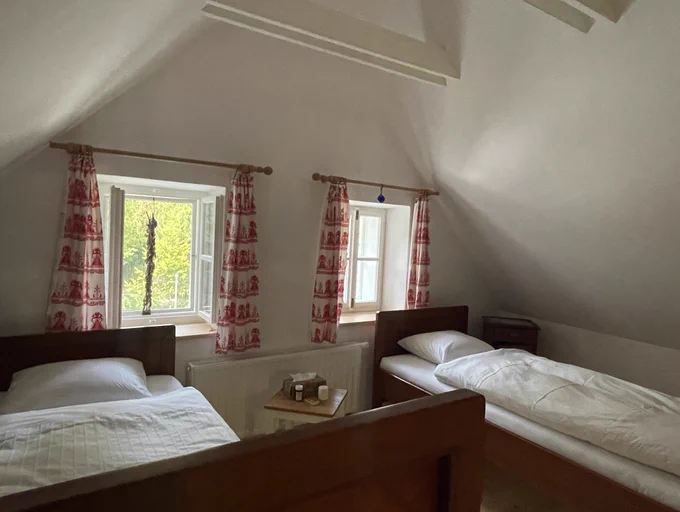 the bedroom with 2 wooden beds and airy ceiling. white painted w red pattern curtains