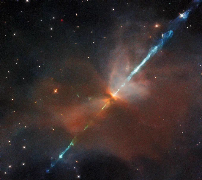A reddish haze of gas and dust is pierced by a diagonal blue filament, against the black backdrop of space.