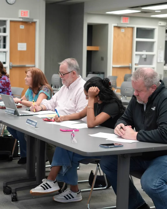 Board members take notes at a table during a Board meeting.