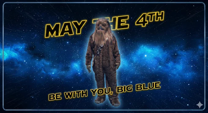 A festive "May the Fourth" graphic with a deep blue starfield and nebula background, framed by a cosmic border. In the center is a full-body character in a detailed Chewbacca costume, wearing a black and grey patterned sash. The text is rendered in the iconic yellow-outlined Star Wars font, with "MAY THE 4TH" in a curve above the character, and the phrase "BE WITH YOU, BIG BLUE" in a straight line below. #TheHamiltonWay