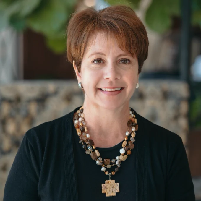 Stacy Keith faces the camera and smiles. She has short reddish hair and wears a multi-strand beaded necklace over a black jacket and blouse. Photo: Lacie Freelen