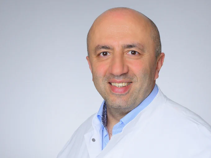 Ein Mann in einem weißen Kittel lächelt freundlich in die Kamera. Prof. Dr. Baki Akgül, Foto: Michael Wodak