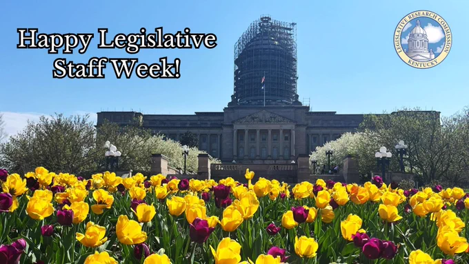 The words Happy Legislative Staff Week! written in the sky of a file photo of the Kentucky State Capitol when the yellow and purple tulips were in bloom. Scaffolding covers the dome. 