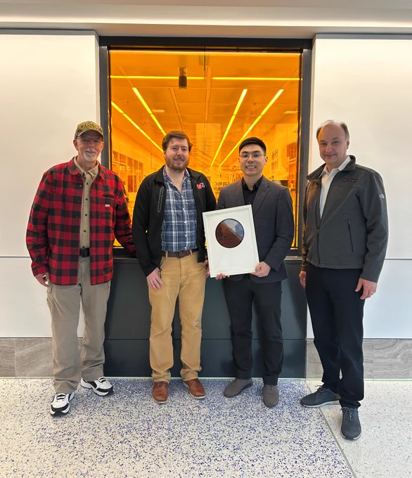 Dennis Grimard, Prof. Kevin O'Brien, Kaidong Peng, and MIT.nano Director Prof. Vladimir Bulović pose outside MIT.nano's cleanroom. Peng holds an 8" wafer etched with a photo of the MIT Dome and the text "Dennis Grimard Distinguished User Award, MIT.nano, April 30, 2026."