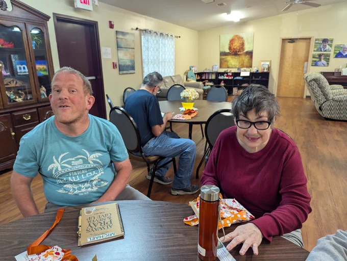 A man and woman with disabilities are seated in a public meeting area for community time.