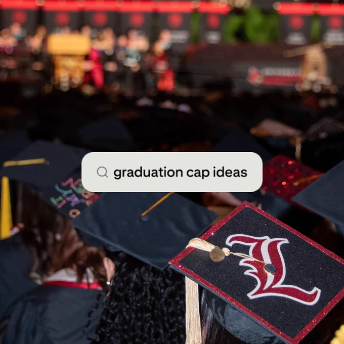 A photo taken from above of UofL graduates sitting at UofL's commencement ceremony, where the top of their caps can be seen with a search bar screenshot over it that reads "graduation cap ideas"