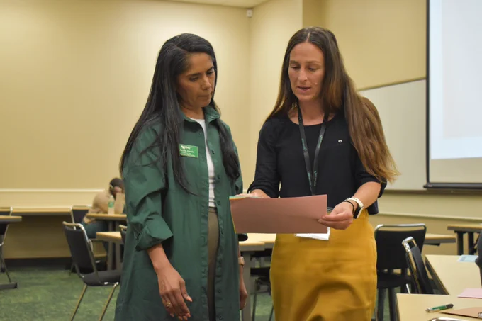 Teaching Hub steering committee member Marissa Zorola and co-director Amy Petros examine a piece of paper during their symposium session.