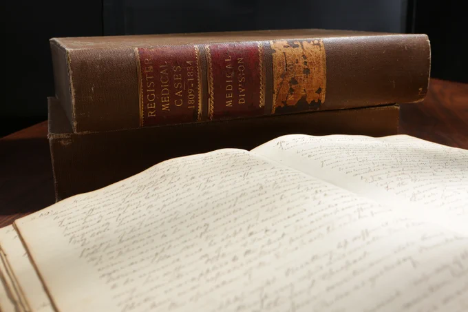 A medical casebook lies open with the case set behind it on the table. The spine reads "Register Medical Cases 1809-1834, Medical Division"