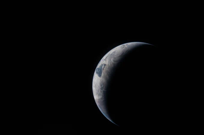 Earth as a thin arc glowing in the darkness of space. Sunlight traces the curves of the ocean and clouds, while the rest of the planet fades into shadow. Credit: NASA