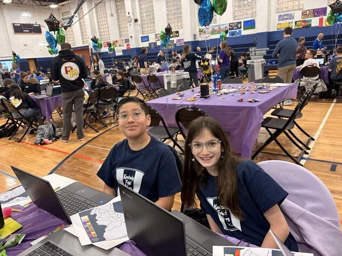 Students sitting at table with laptops, smiling together.