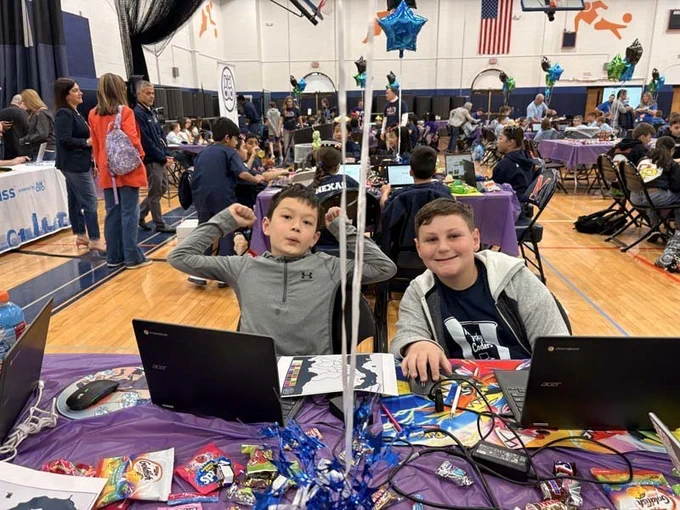 Students sitting at table with laptops, smiling together.