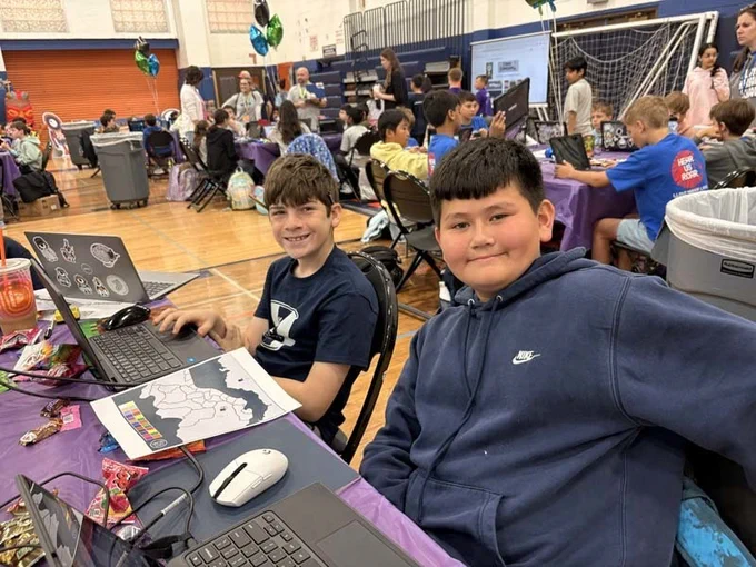 Students sitting at table with laptops, smiling together.