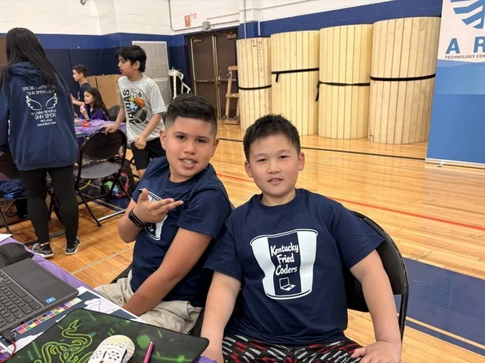 Students sitting at table with laptops, smiling together.