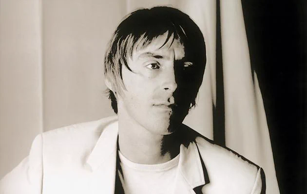 Paul Weller in a black and white portrait during the Stanley Road era, wearing a light blazer and looking off to the side with a calm, focused expression
