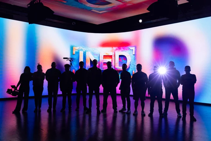 Silhouettes of a group pose in front of a colorful, neon-lit backdrop with the letters "INED" prominently displayed.