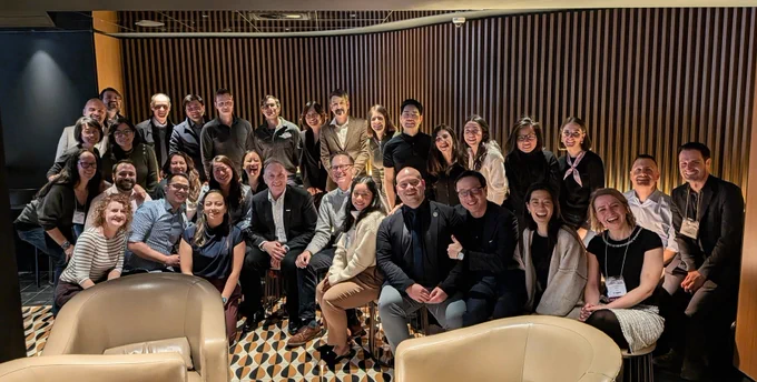 A group of 33 people posed together and smiling in a lounge setting.