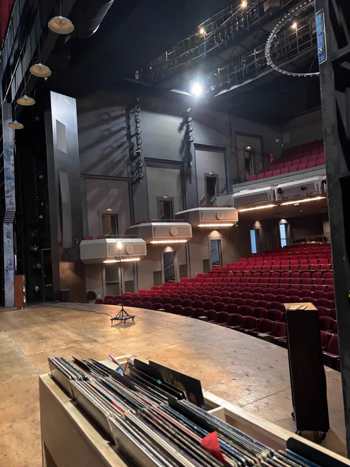 Image from the perspective of the theatre stage, with rows of red seats and theatre headlights. 