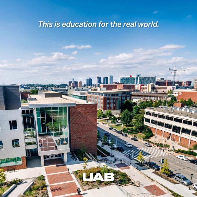 The image shows an aerial view of the University of Alabama at Birmingham (UAB) campus with modern buildings, streets, and greenery. The cityscape of Birmingham is visible in the background under a blue sky with clouds. A caption at the top reads, "This is education for the real world." The UAB logo is at the bottom.